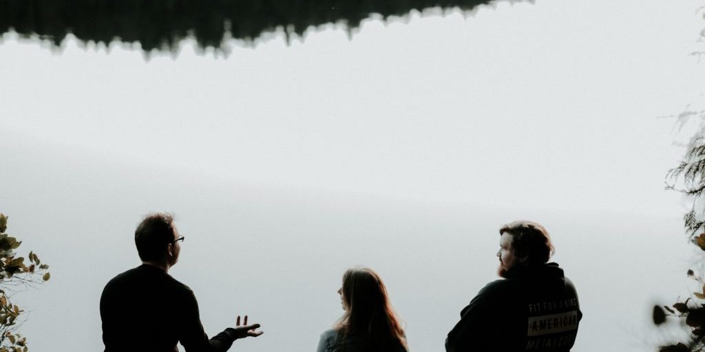 silhouette of three people sitting on cliff under foggy weather